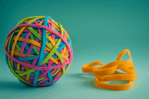 Colorful rubber band ball with loose yellow bands beside it on white background — symbolizing organization and flexibility in CVOR audit preparation