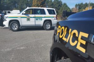 An Ontario Ministry of Transportation (MTO) enforcement vehicle and an Ontario Provincial Police (OPP) cruiser parked side by side in a lot during a roadside inspection operation under clear skies.