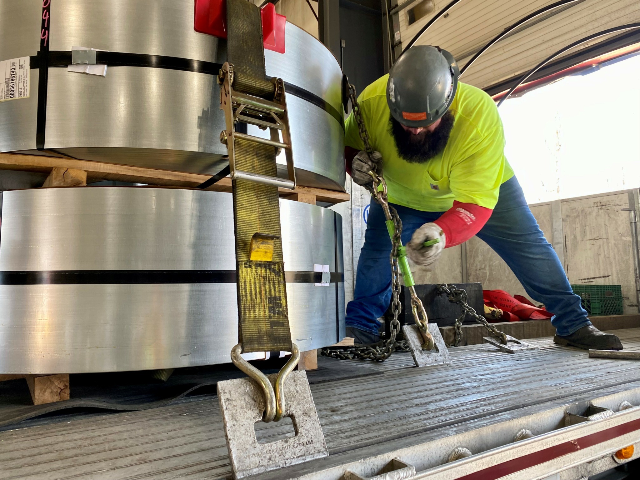 Commercial driver securing a heavy steel coil load with chains and straps, demonstrating proper cargo securement practices under Red Seal commercial driver standards in Canada.